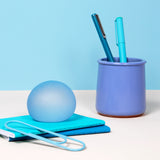 Pale blue Dew Speks Gump Original stress ball on a teal notebook beside a pen pot and paperclip