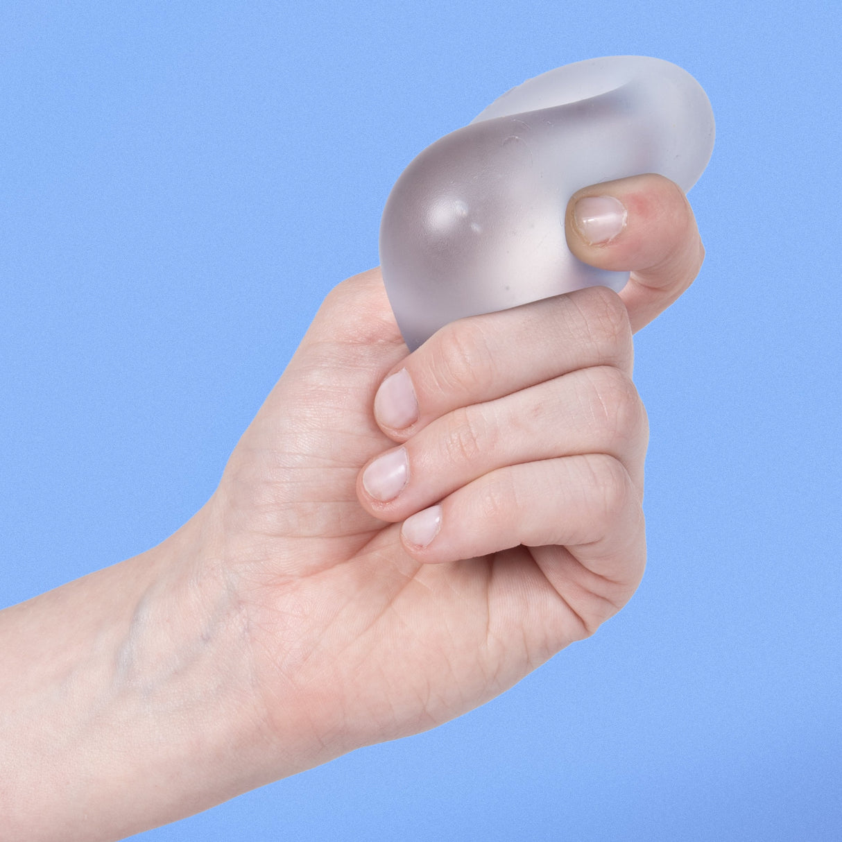 Hand squeezing a pale blue Dew Speks Gump Original memory gel stress ball against a blue background