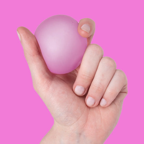 Hand holding a pink Moon Jelly Speks Gump Original memory gel stress ball against a pink background