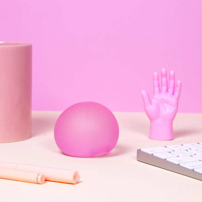 Pink Speks Gump Original memory gel stress ball on a desk beside a keyboard and decorative hand ornament against a pink background