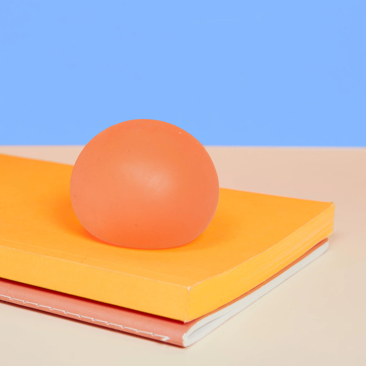 Coral orange Reef Speks Gump Original stress ball resting on a yellow notebook against a blue background