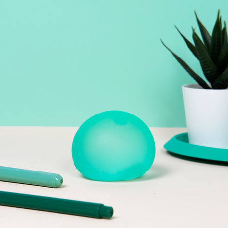 Teal Sea Glass Speks Gump Original stress ball on a desk beside pens and a succulent plant