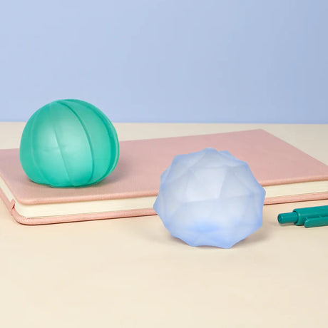 Teal and pale blue Speks Gump Surface stress balls displayed on a notebook beside pens on a desk