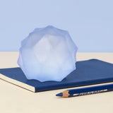 Pale blue Speks Gump Surface stress ball resting on a navy notebook beside a pencil