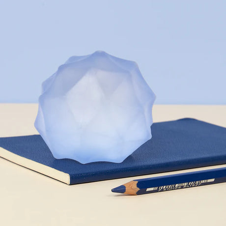 Pale blue Speks Gump Surface stress ball resting on a navy notebook beside a pencil