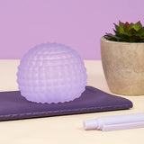 Purple Speks Gump Surface stress ball resting on a notebook beside a marker pen and succulent plant