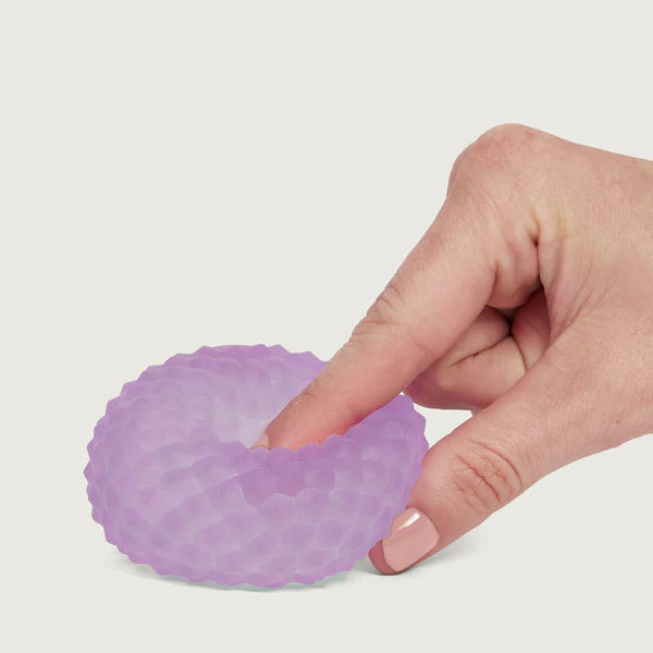 Hand pressing and stretching a purple Speks Gump Surface memory gel stress ball flat