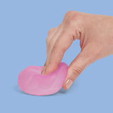 Hand pressing and stretching a pink Speks Gump Surface memory gel stress ball flat on a blue surface