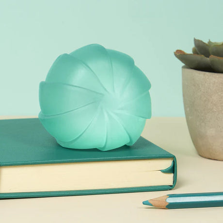 Teal Speks Gump Surface stress ball resting on a book on a desk beside a succulent plant