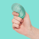 Hand squeezing a teal Speks Gump Surface memory gel stress ball against a teal background
