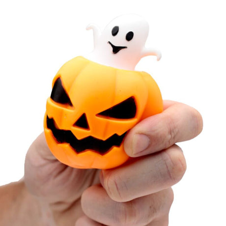 A hand holding a small Halloween squishy toy shaped like an orange jack-o'-lantern pumpkin with a white ghost popping out from the top, against a plain white background.
