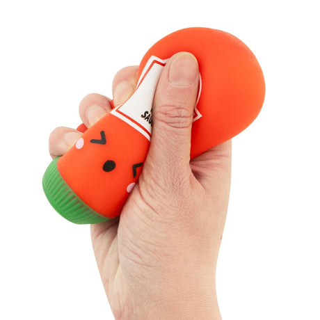 Hand squeezing a red kawaii hot sauce squishy bottle fidget toy, showing the satisfying squish