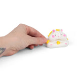 Hand pressing yellow pom pom onto the sticky surface of the Scrunchems Squishy Hamster
