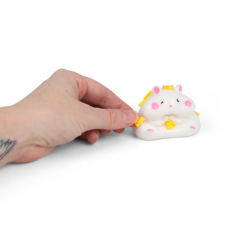 Hand pressing yellow pom pom onto the sticky surface of the Scrunchems Squishy Hamster
