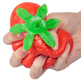 Hand squeezing a red gel-filled strawberry stress toy, showing the satisfying squish and stretch