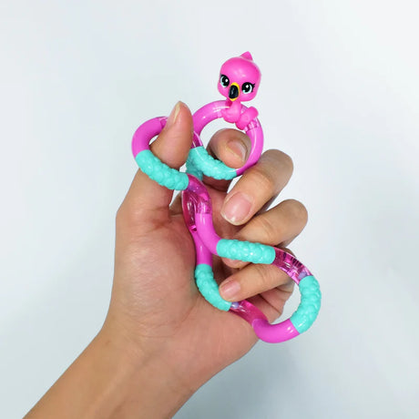 Hand holding a pink and teal flamingo Tangle Jr. Pet fidget toy in a loose grip