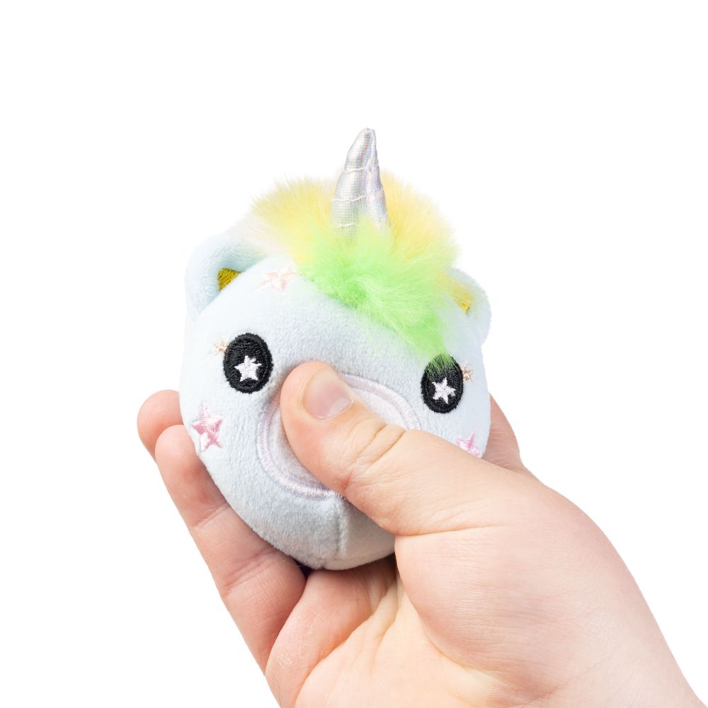 Hand squeezing a blue rainbow-mane unicorn plushie sensory toy to show compact palm-sized size