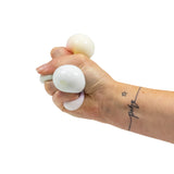 Adult hand squeezing three pearlescent white squish balls, demonstrating their stretchy give